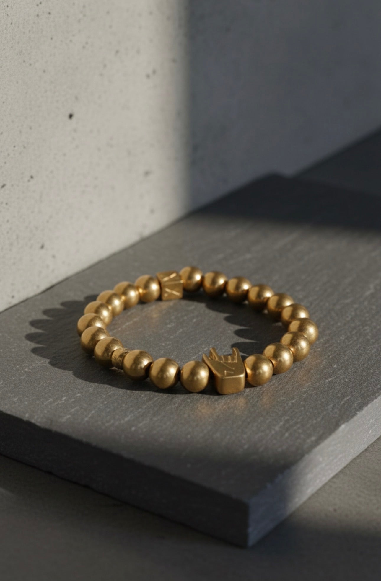 Close-up of a gold bead bracelet featuring a unique hand-shaped charm, elegantly displayed on a dark stone surface with soft natural lighting, showcasing The Little Icons - Manus Ferox.