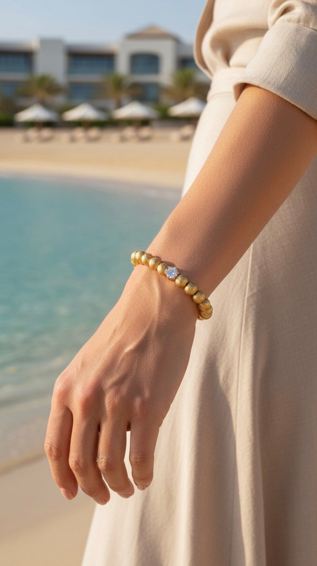 Limited Edition - Textura Aurea Imperia bracelet featuring gold beads and a central sparkling gem, elegantly worn on a wrist by the beach in soft natural light.