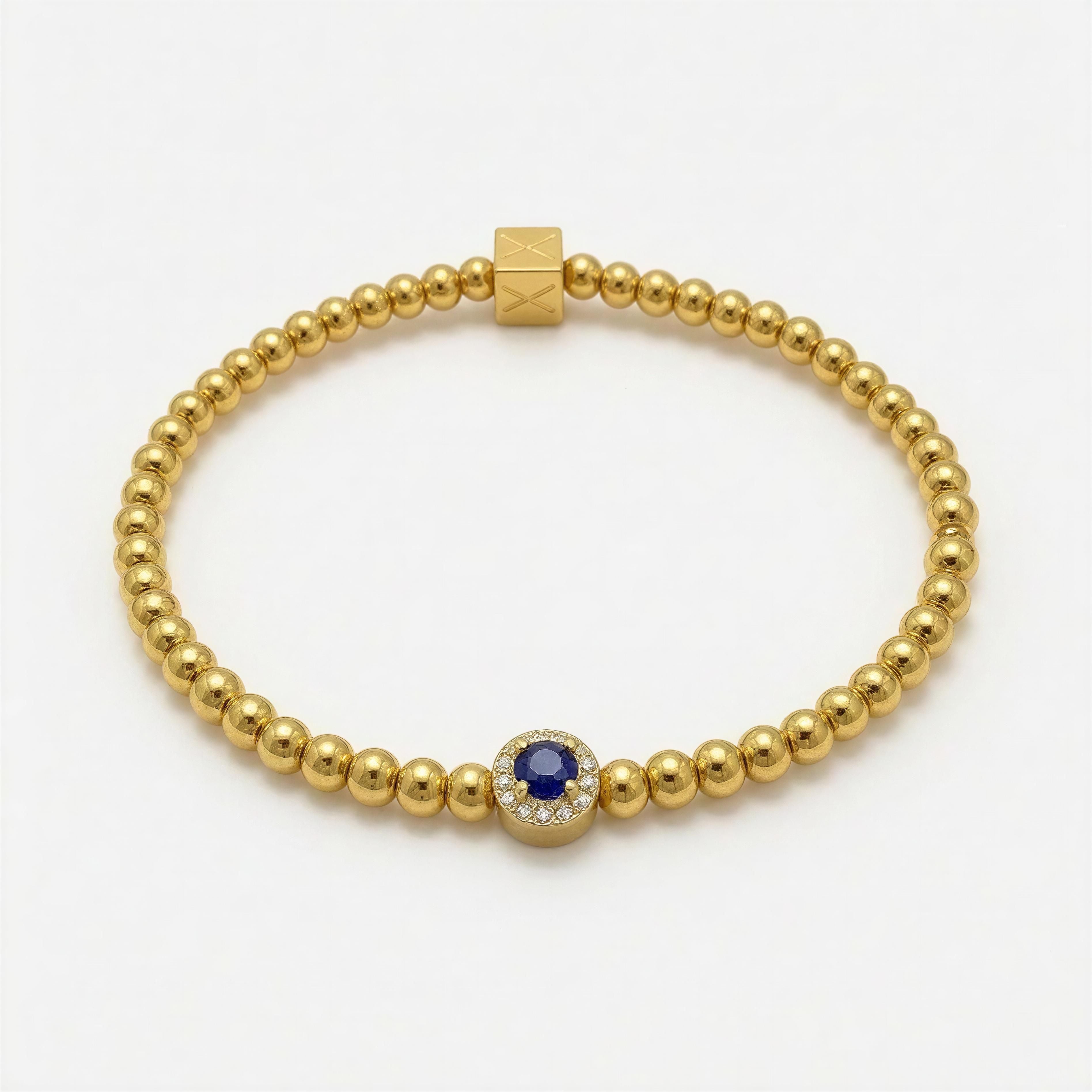 XX ÉLÉGANCE - AZURA ROYALE gold beaded bracelet featuring a central blue gemstone encircled by small clear stones, combining handcrafted luxury with elegant simplicity.