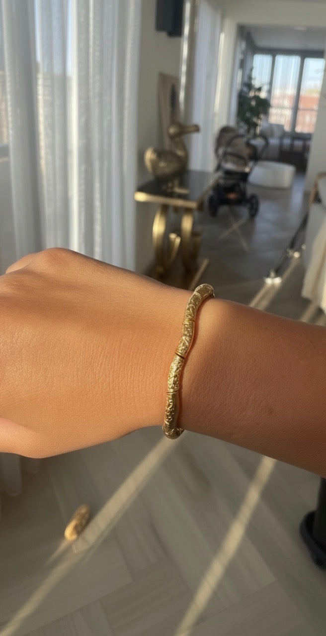 Close-up of a hand wearing a textured gold bracelet from The Essential Collection - Essentia Aurea, featuring intricate detailing in warm natural light.