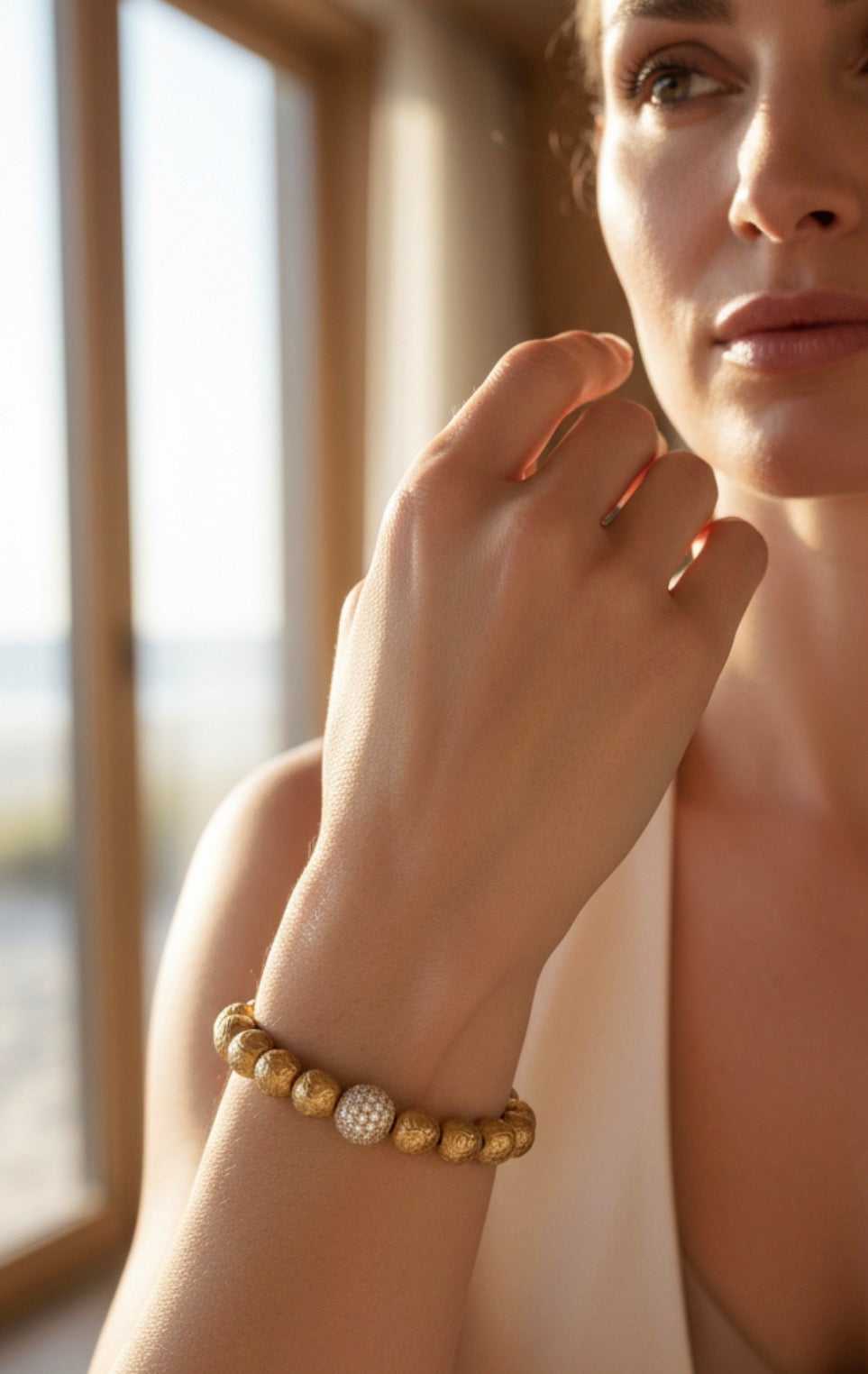 Elegant close-up of a woman wearing the Limited Edition - Orbis Aurea Imperium bracelet featuring goldleaf beads and a sparkling central bead, bathed in natural light.
