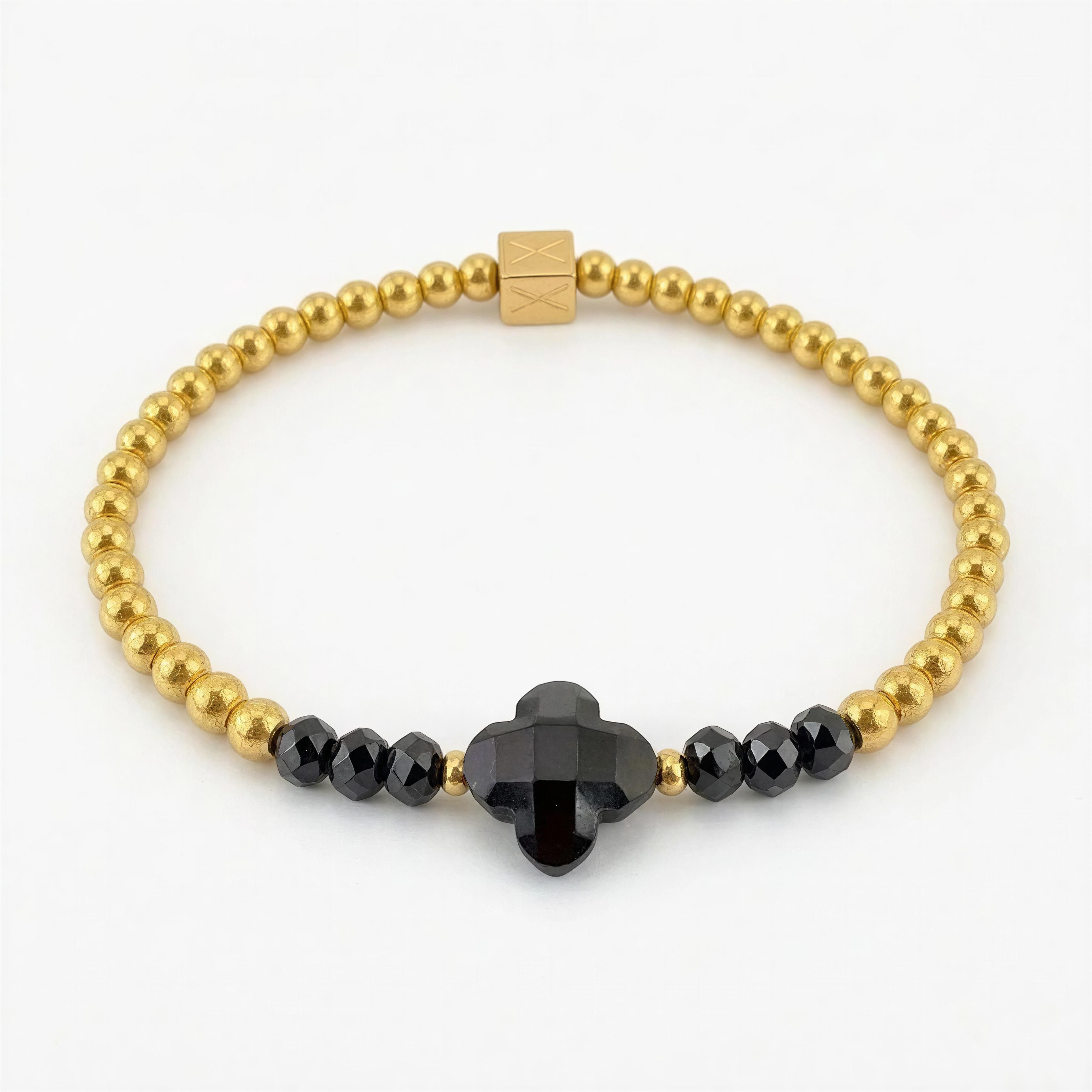 Close-up of a luxury XX Élégance - Midnight Clover bracelet featuring polished gold beads and a central black clover-shaped gemstone with faceted black beads on either side.