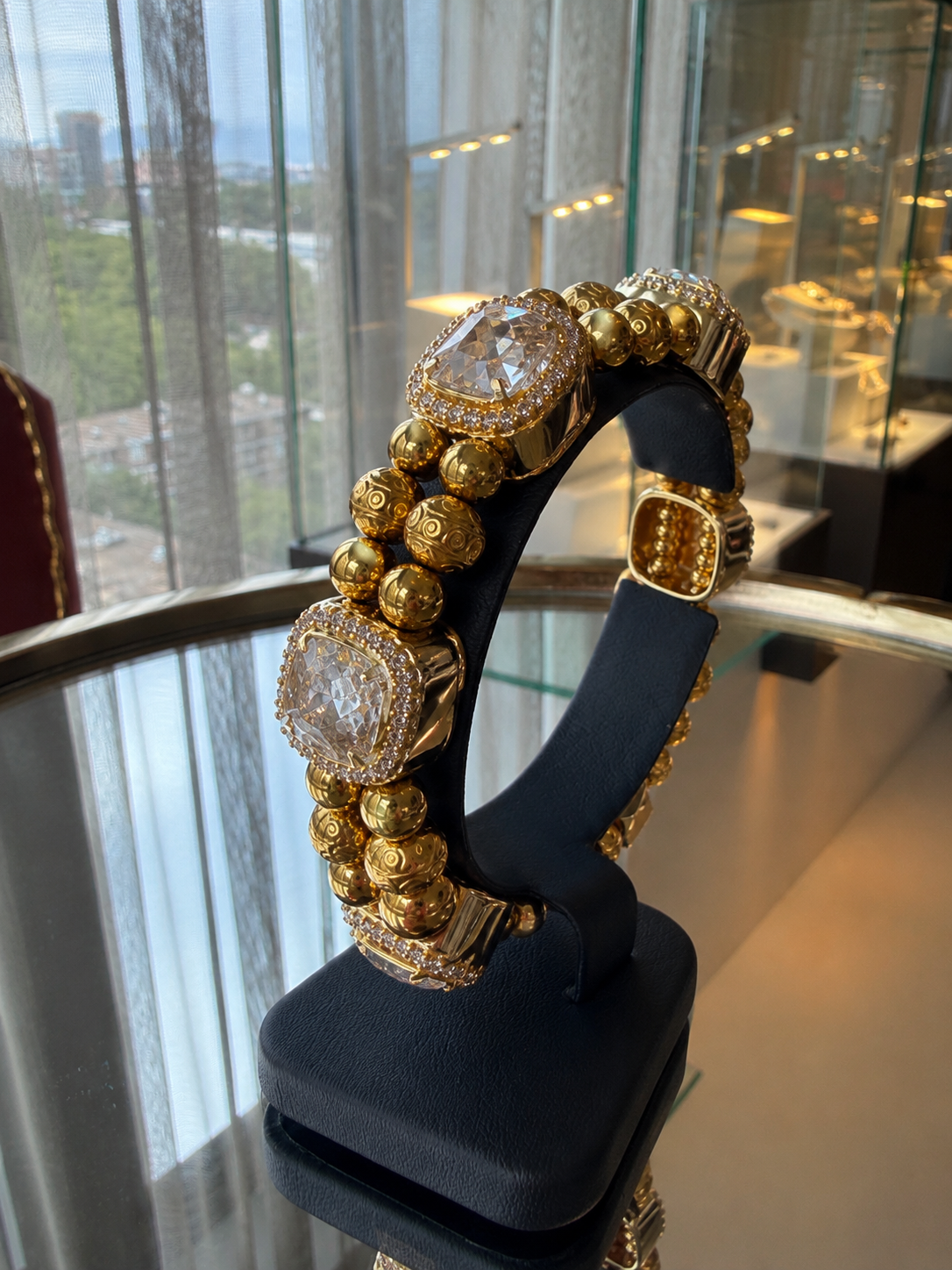 XX ÉLÉGANCE – LIMITED EDITION gold beaded bracelet featuring large clear crystals and intricate gold detailing, displayed on a black stand in a luxury setting.